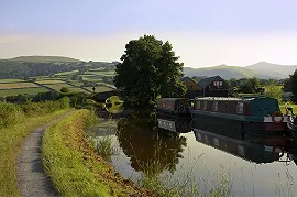 Narrowboats moored on the Mon & Brec canal with a bridge and hills in the distance