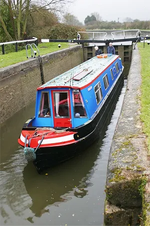 A couple on a canal boat holiday onboard inside a canal lock onboaard a coloutful narrowboat fom wyvern shipping.